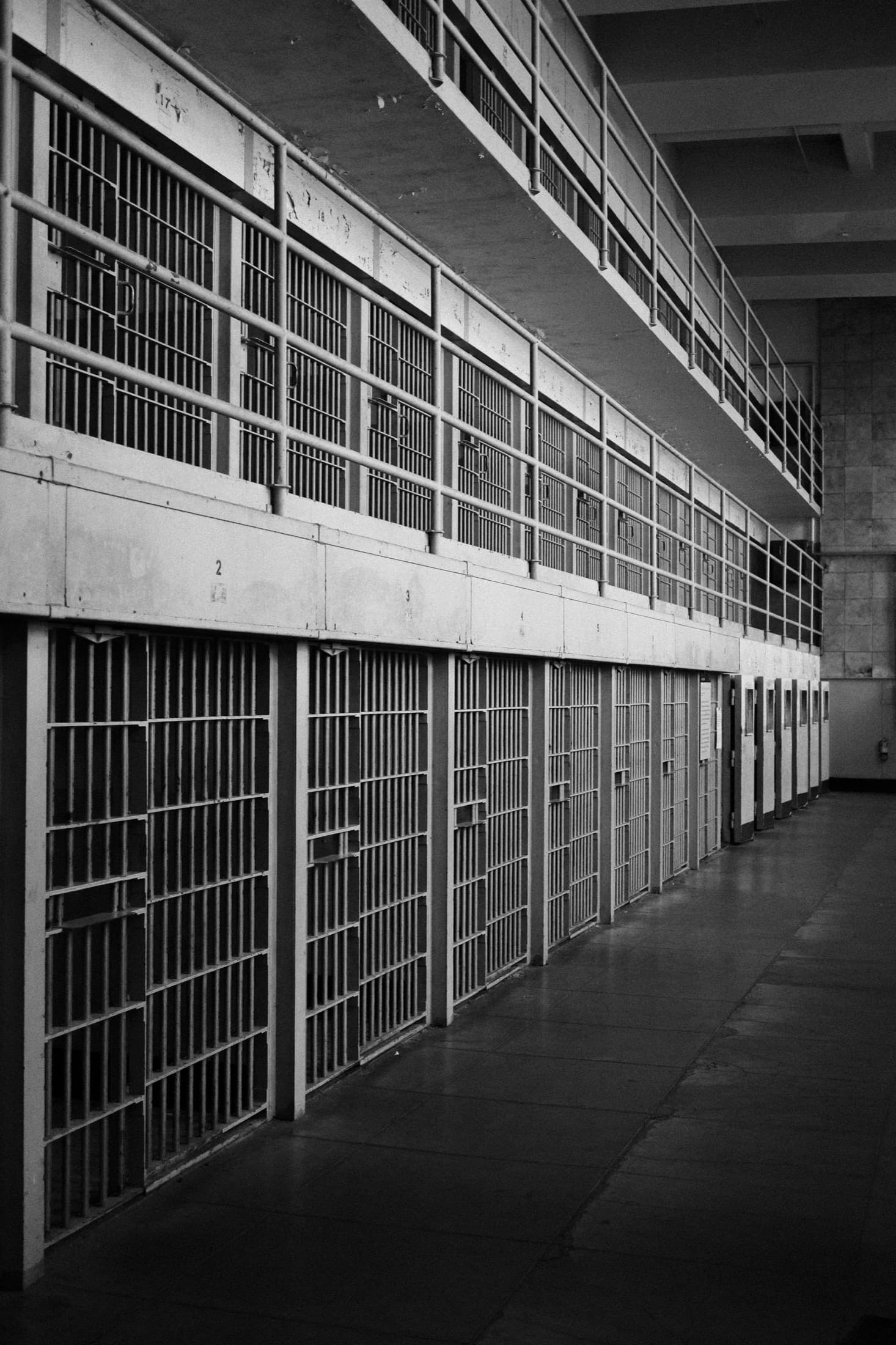 Black-and-white row of barred cell doors along an empty walkway